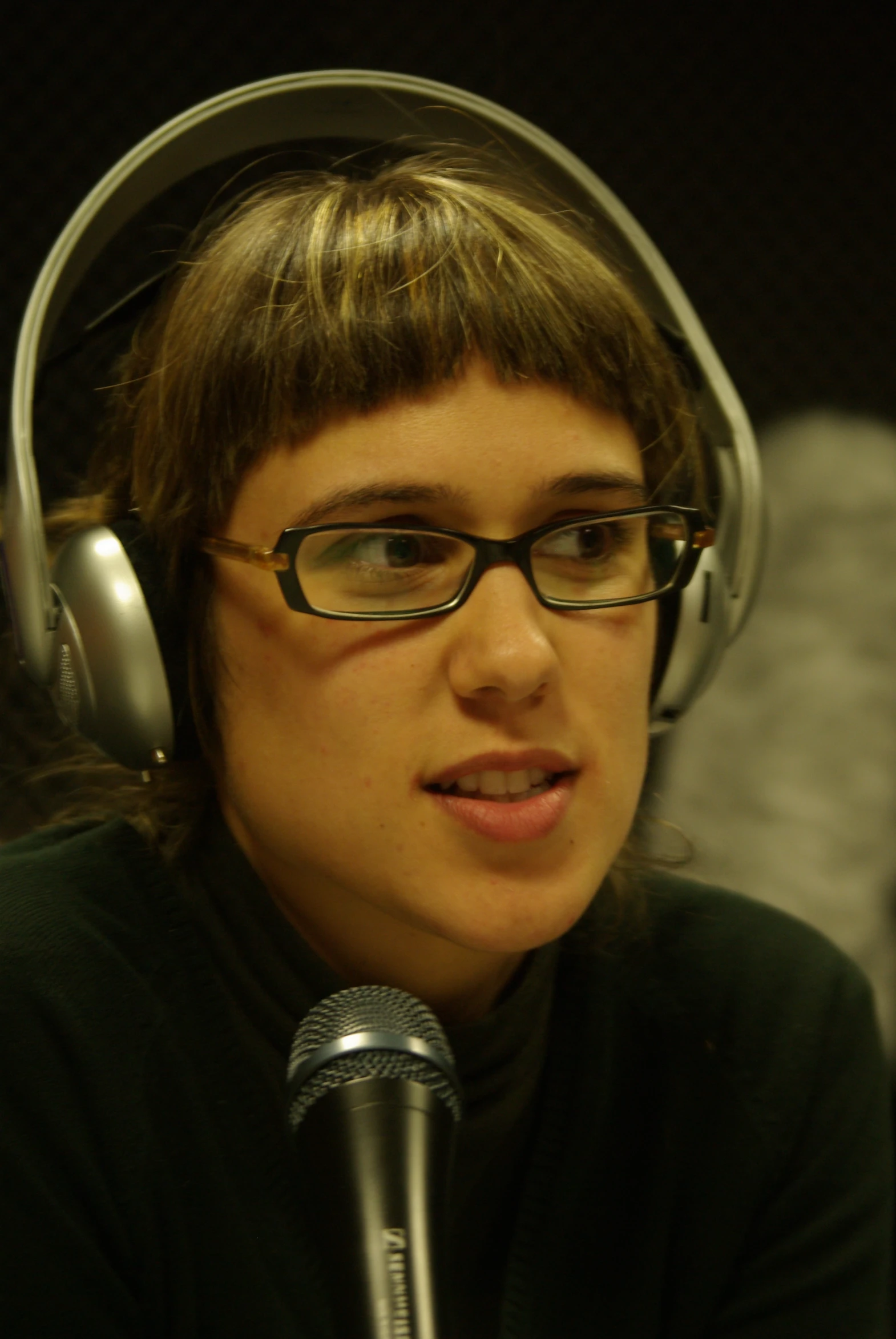 woman in glasses with headphones on speaking into a microphone