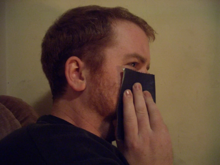 a man with his face near a piece of paper that he is holding to his nose