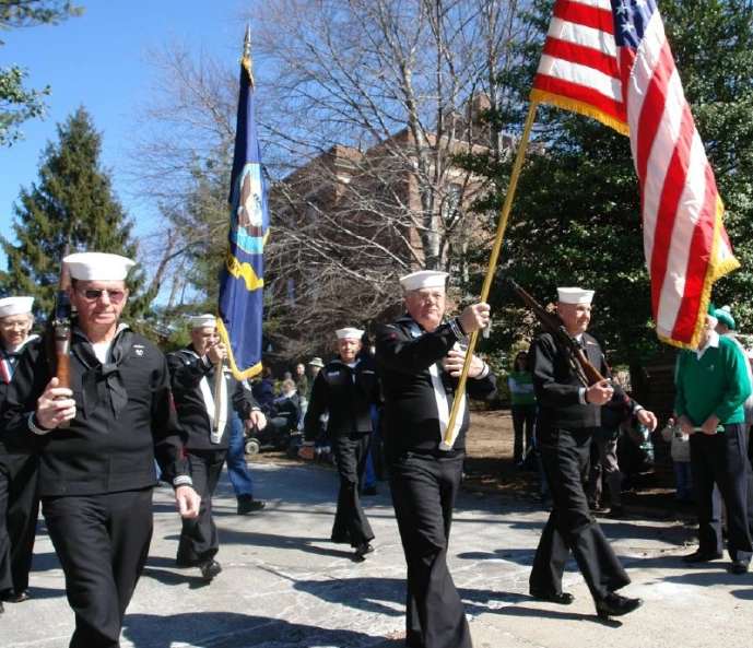 several men in navy uniforms carry flags and walk down a street