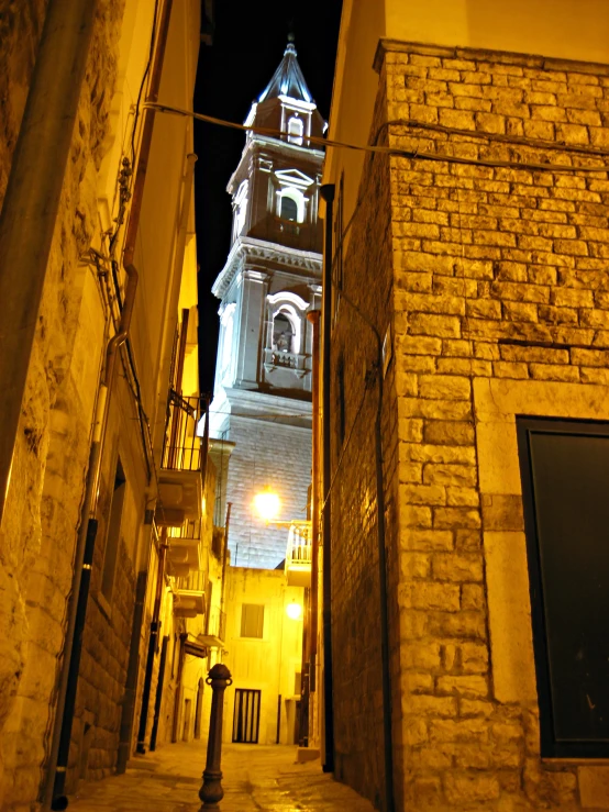 a church tower is visible through the cobblestone streets at night