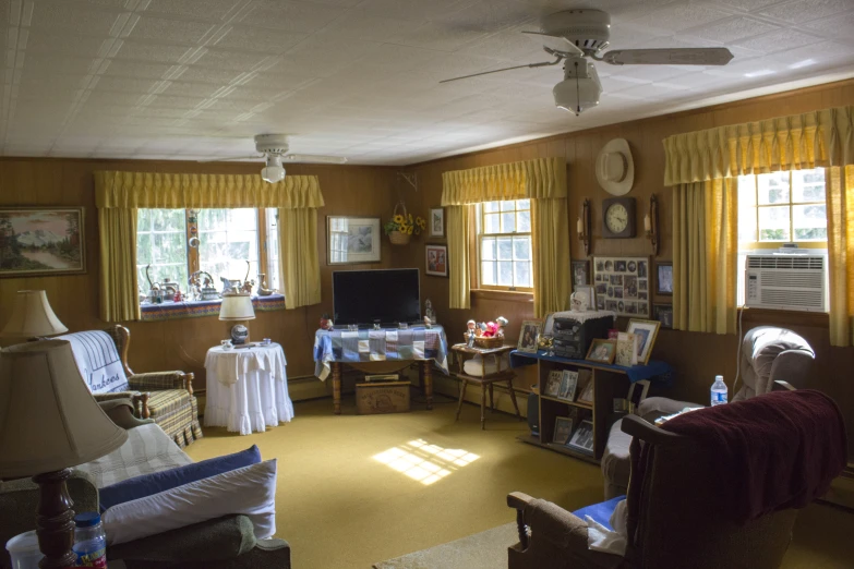 a very cluttered living room with yellow ds and sun shining through the windows