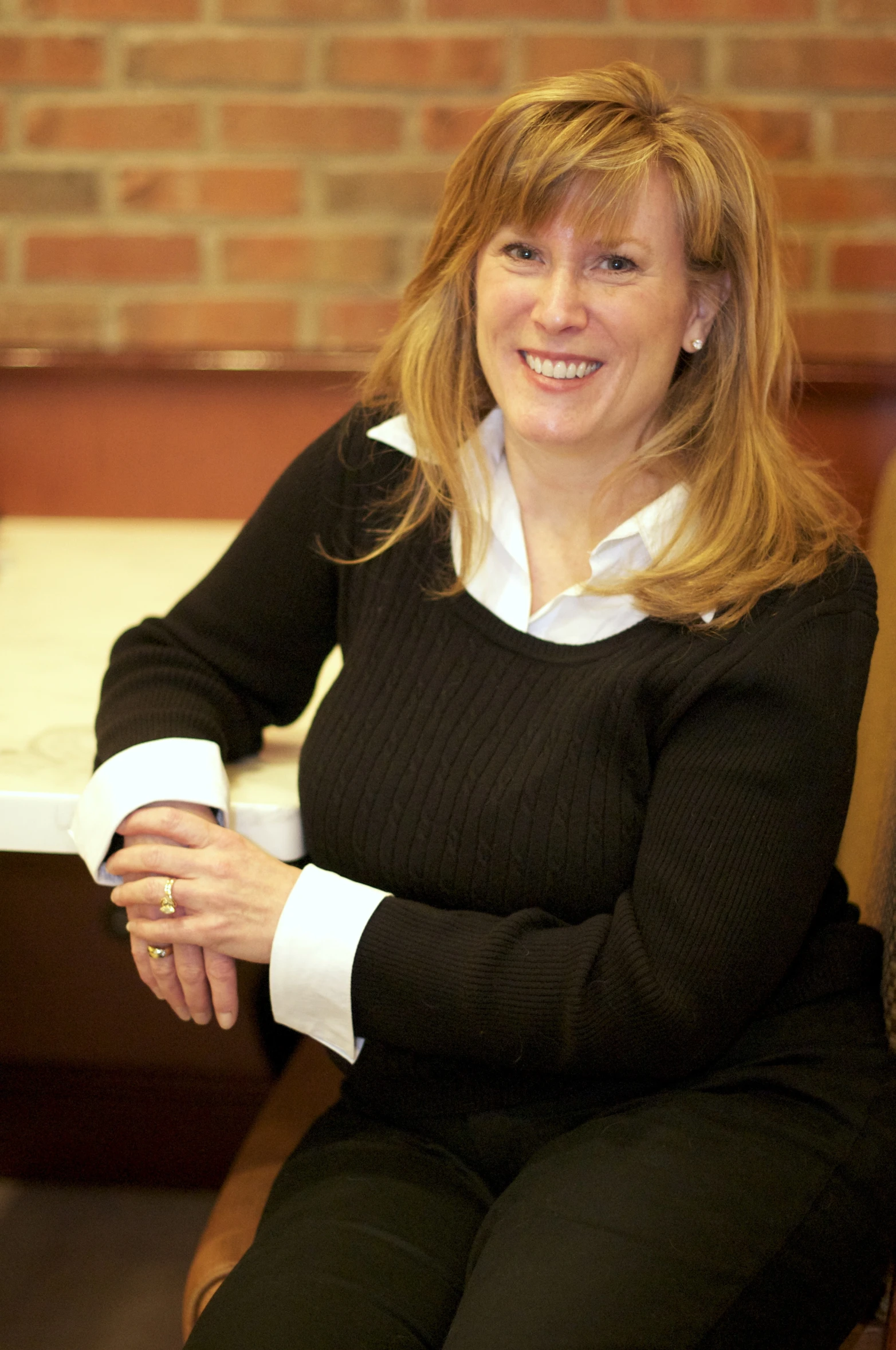 a smiling lady is posing in front of a brick wall