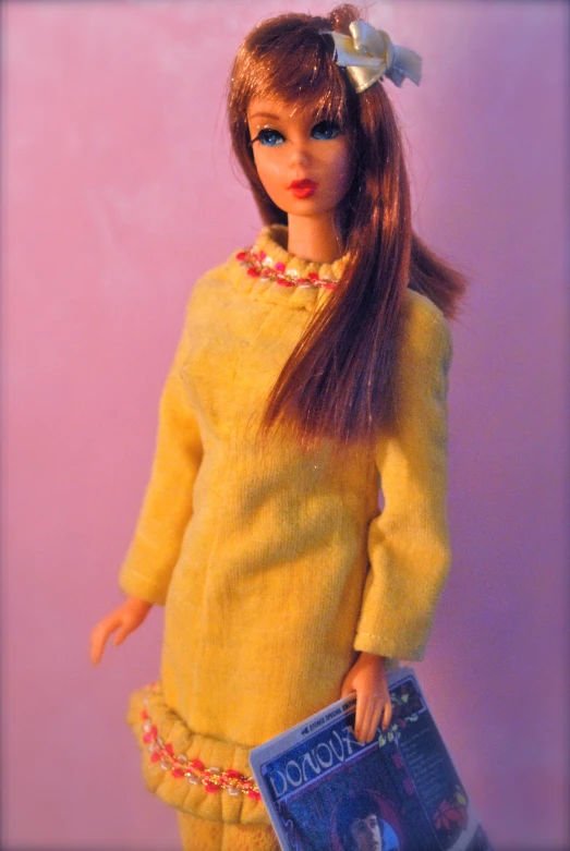 a doll wearing a yellow dress holding a magazine