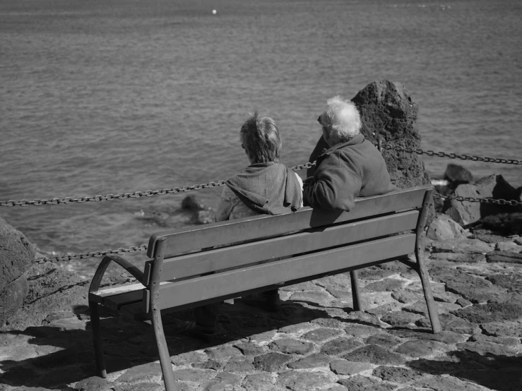 black and white pograph of a man and woman sitting on a bench by the water