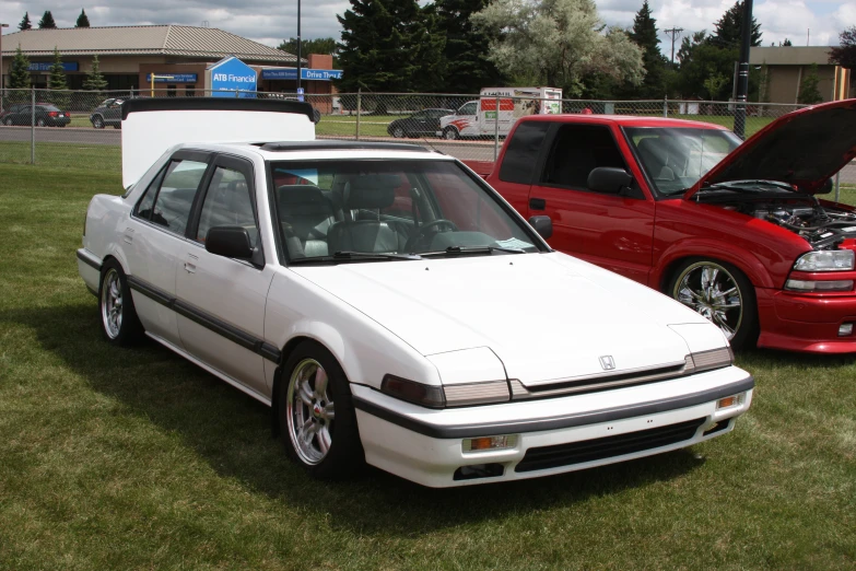 a white car sits parked on a grassy field next to other cars