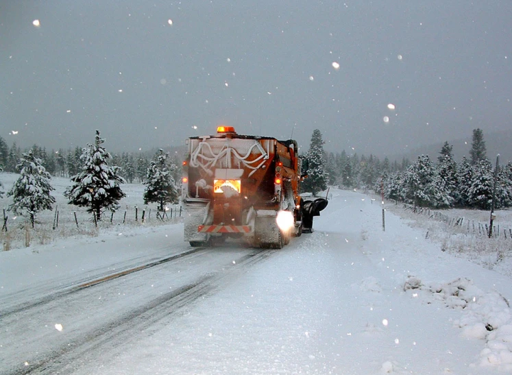 a big orange truck driving on a road through the snow