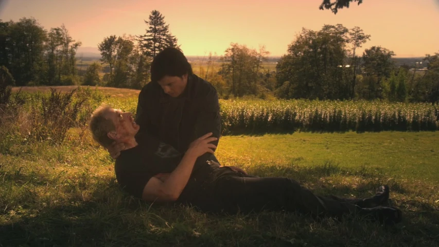 a person laying down while another man kneels in the grass