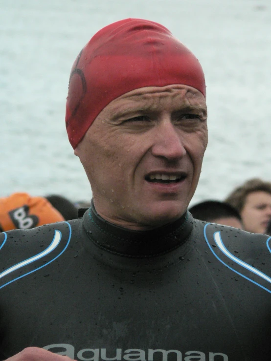 man in wetsuit with red cap and other onlookers