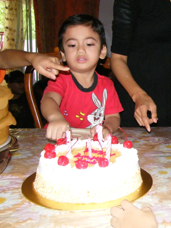 the  in red shirt is sitting at the table blowing out candles