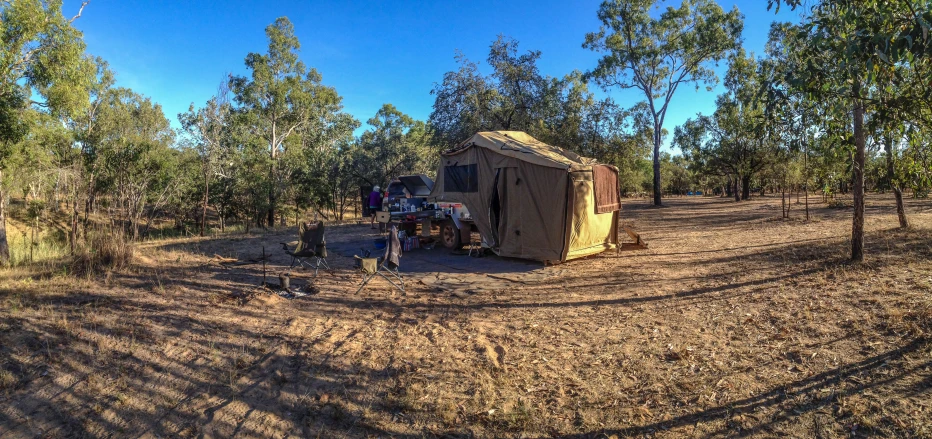 a small camper in the woods with people standing around it