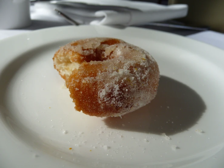 a white plate with a single sugar coated doughnut