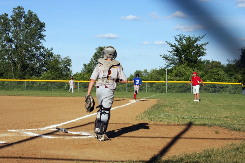 a little league game with the catcher walking into home plate