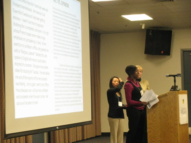 three women are standing behind a podium speaking at the podium