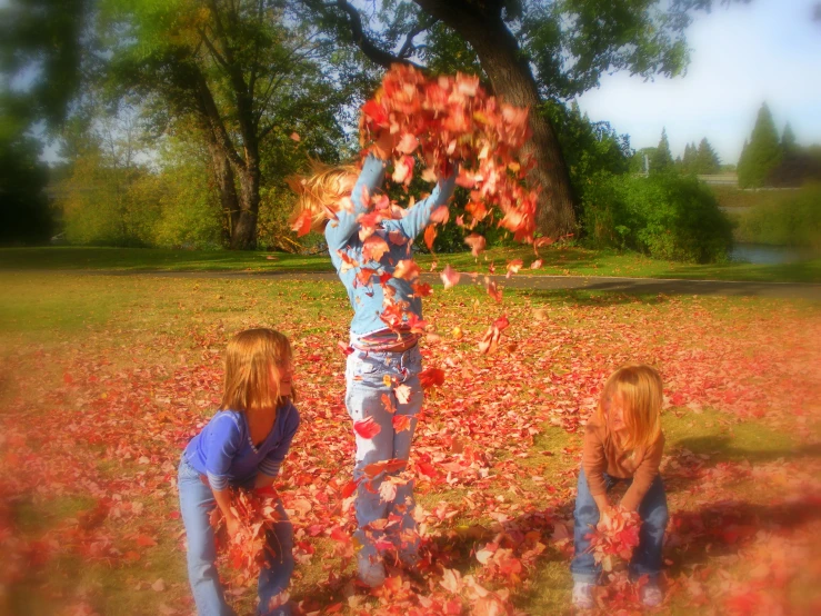 two girls and a man standing in front of a tree in a park full of leaves