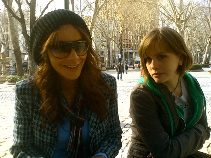 two girls sitting in a sidewalk in front of some trees