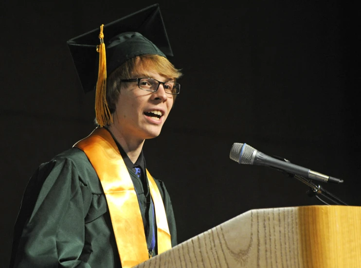 a man wearing a graduation hat speaking at a podium