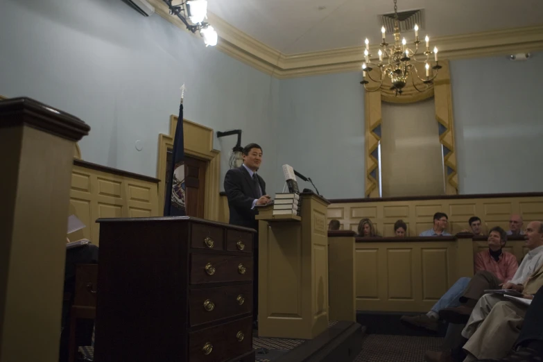 man standing behind podium reading to people in front of him