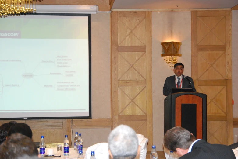 man standing in front of a screen speaking at a public event