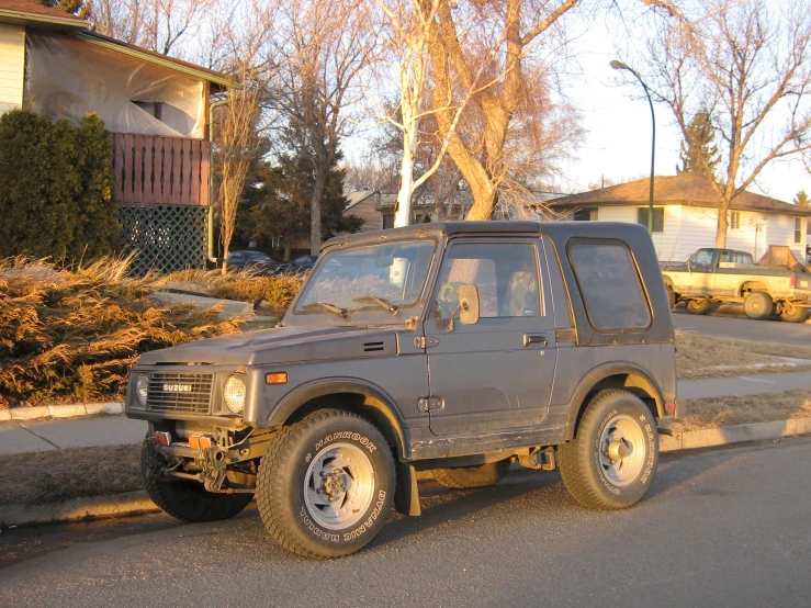 an older grey four door jeep parked on the side of a street