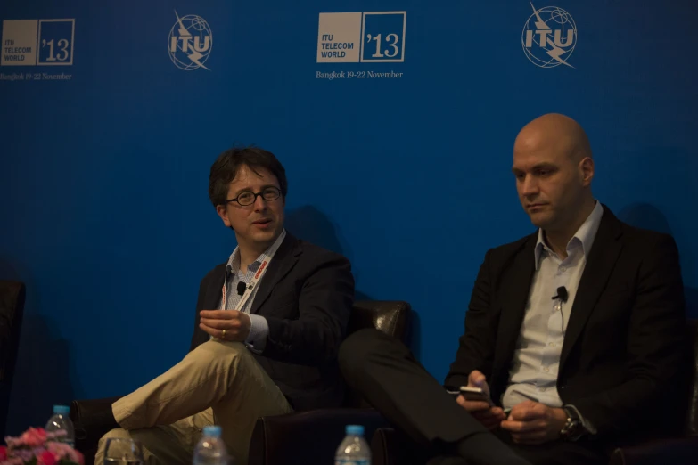 two men sitting next to each other in front of blue backdrop