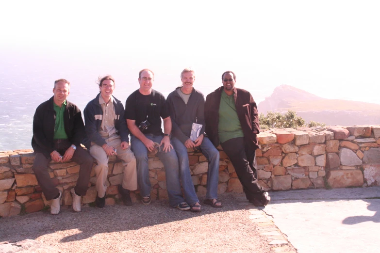 a group of men sitting on a stone wall next to the ocean