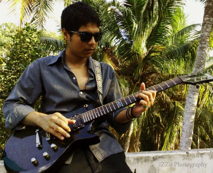 a man playing an electric guitar in front of some palm trees