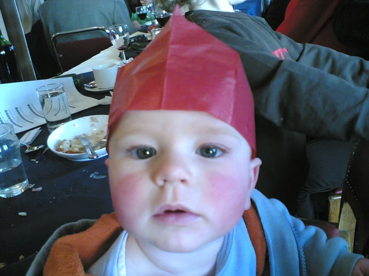 a toddler wearing a paper hat and looking at the camera