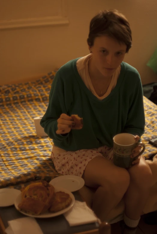 a woman holding a cup in front of her while sitting on a bed