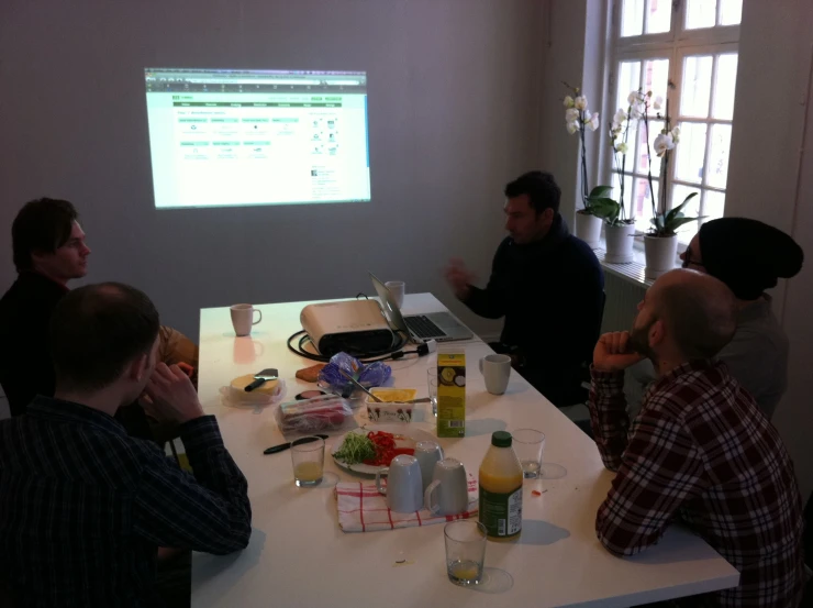 four men sitting around a table with a projector screen