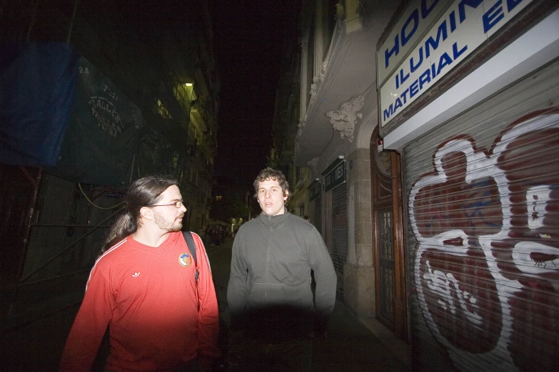 two men standing next to each other on a dark alley way