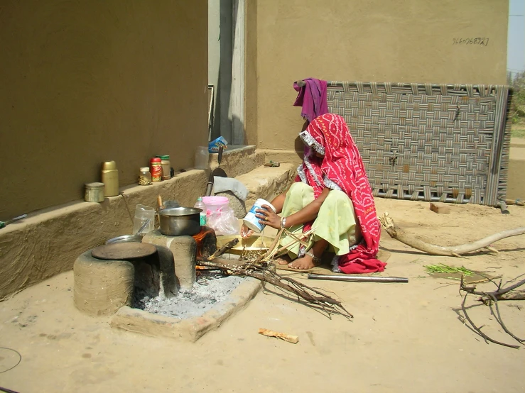 a woman with a pink head covering sitting outside near an oven