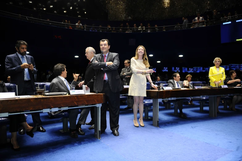 three people stand near the desks of two men and two women