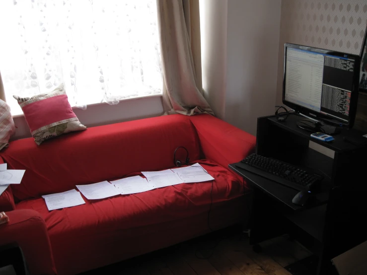 a red couch with papers on it sits in front of a computer monitor