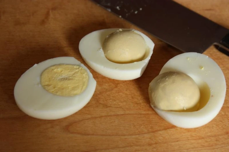 three hard boiled eggs sitting next to a knife on top of a  board