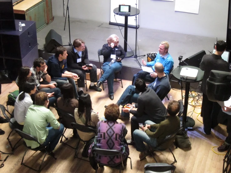 group of people sitting in chairs near a stand talking