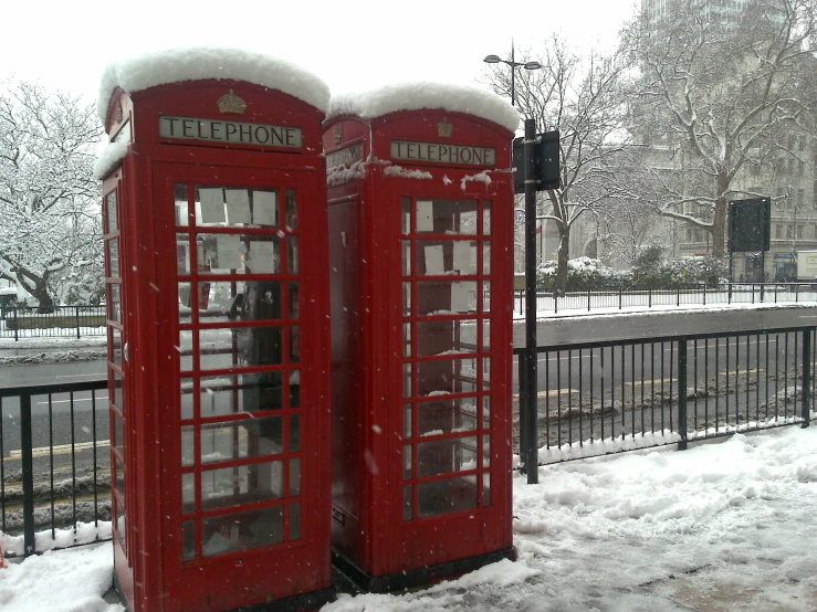 two red telephone booths sitting next to a fence