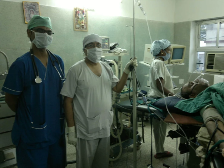 three medical workers stand around a man laying on a hospital bed