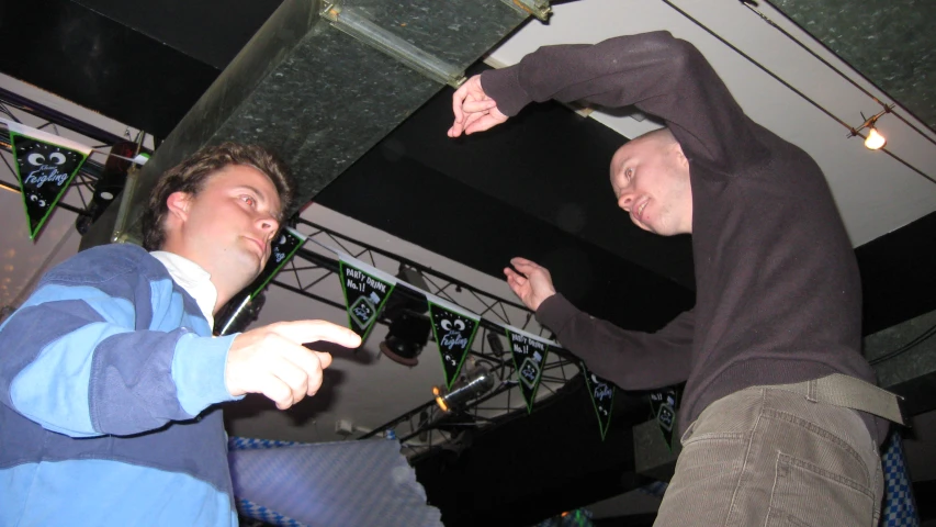 two young men standing in a room with one pointing at the ceiling