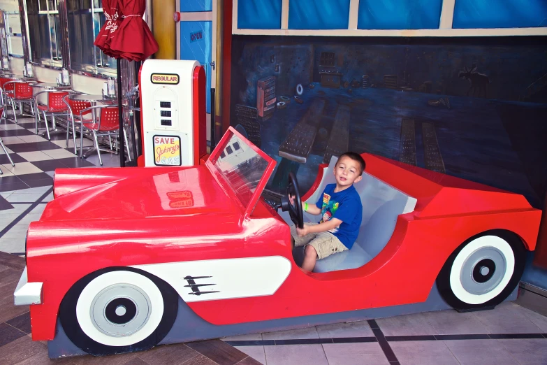 a child in a small red race car with gas pumps
