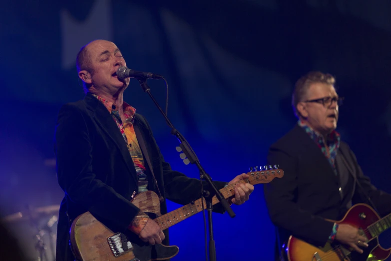 two men with guitars on stage with microphone