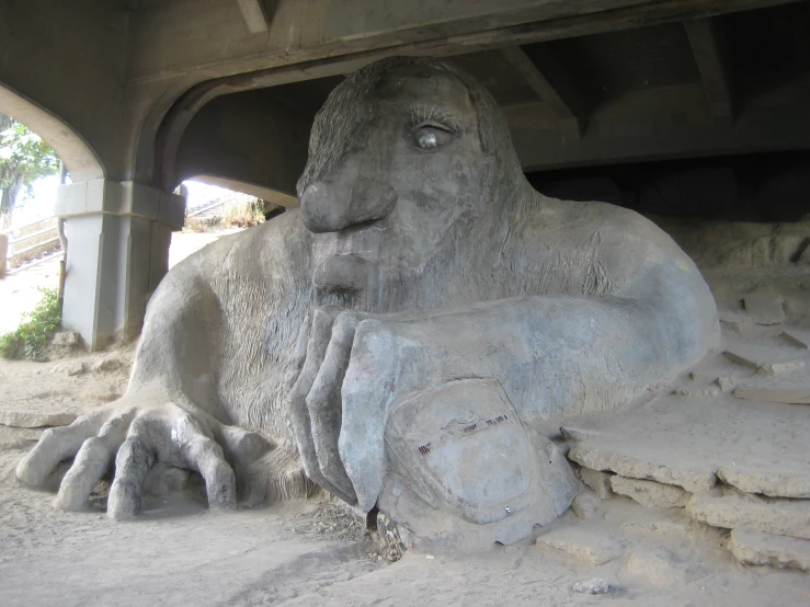 a large concrete statue with arms and hands under a bridge