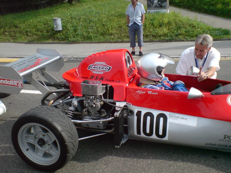 a woman sitting in a race car with a man next to it