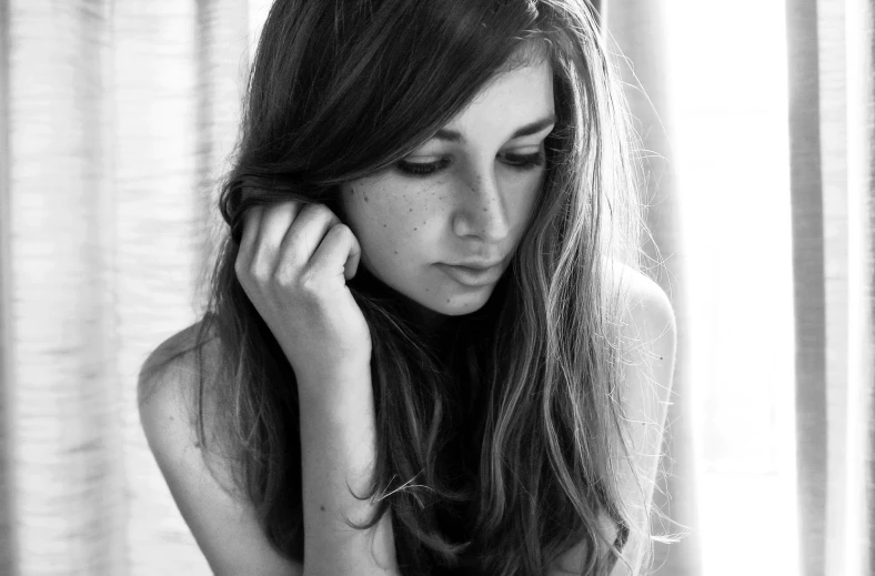 a woman is sitting by the window and looking down at her hair