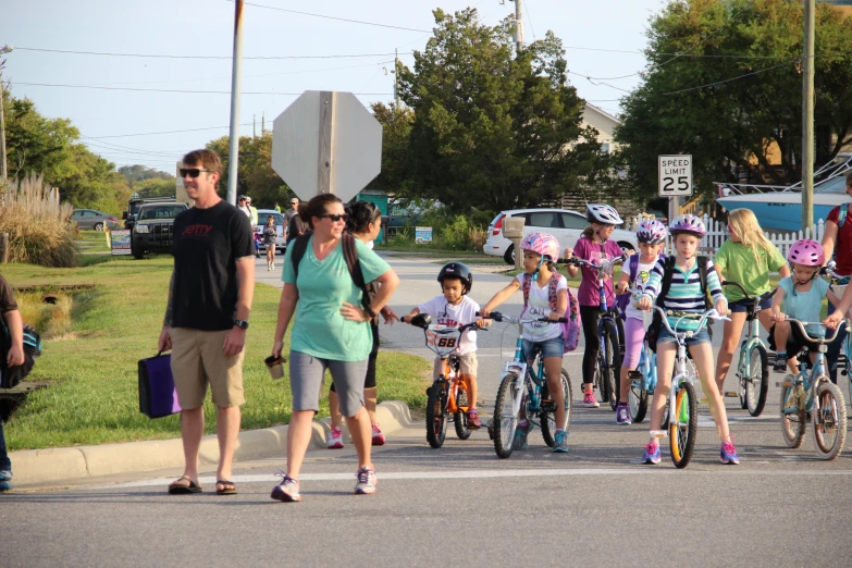 some children riding bicycles down the road while adults watch