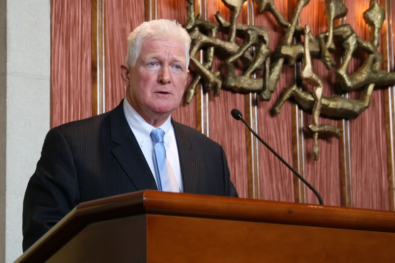 the man is standing at a podium wearing a suit