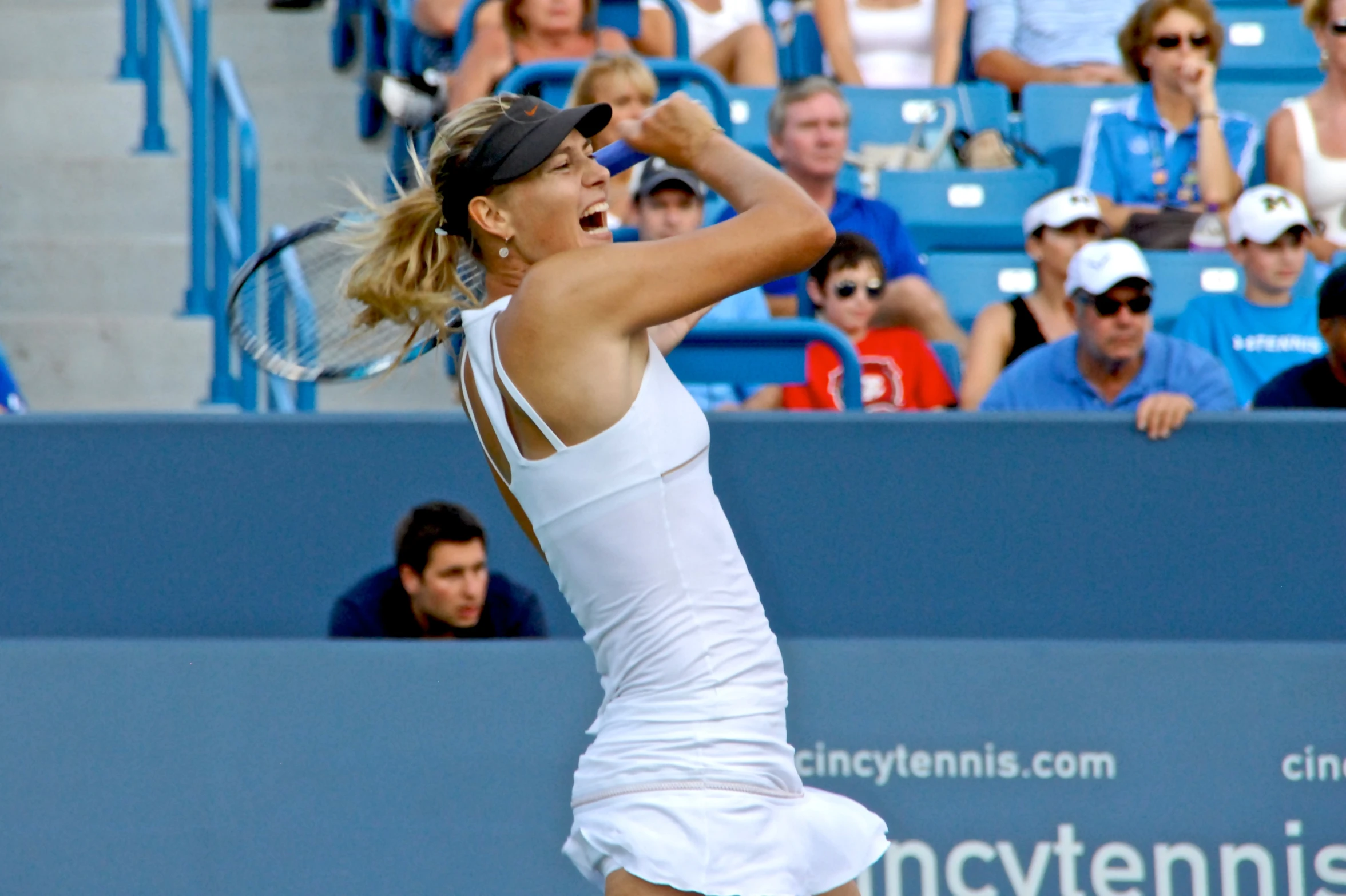 woman in white dress swinging tennis racket at ball