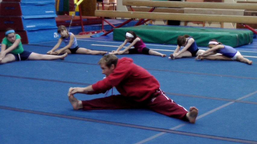 a woman sitting on a gymnastics floor in front of other girls