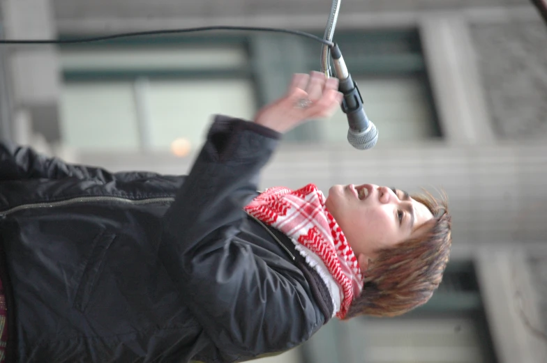 a woman in a scarf stands at a microphone while speaking