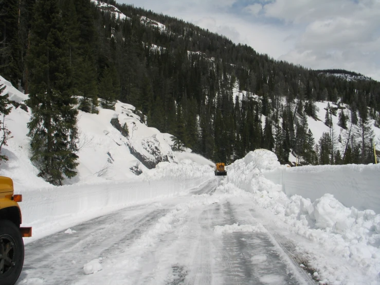 a truck driving down the snowy road near a snowy mountain