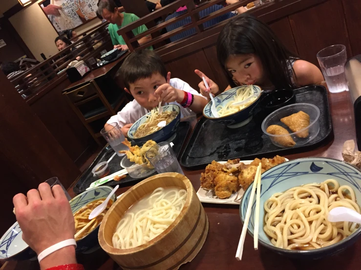 a woman and two children eating noodles in a restaurant